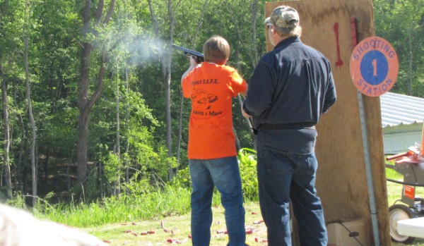 Male Shotgunner just after shot with smoke from gun, male coach looking on